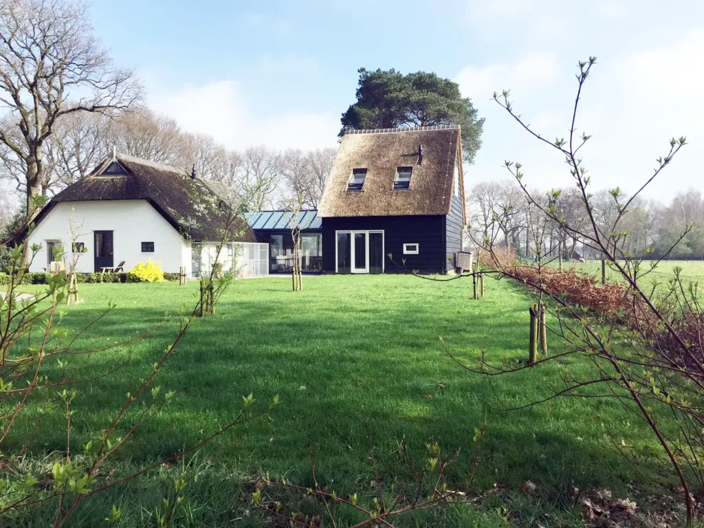 Het woonhuis met rieten dak en het donkere gastenverblijf aan een groot gazon in Ruinen